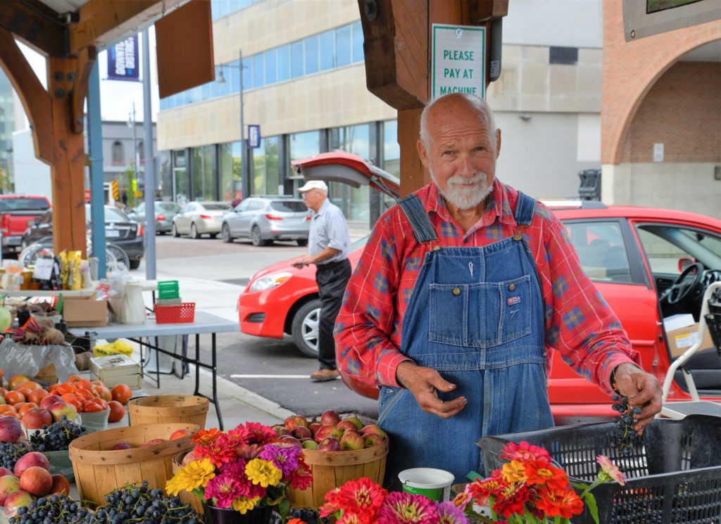 A vendor at the Farmers Market selling fruits and flowers